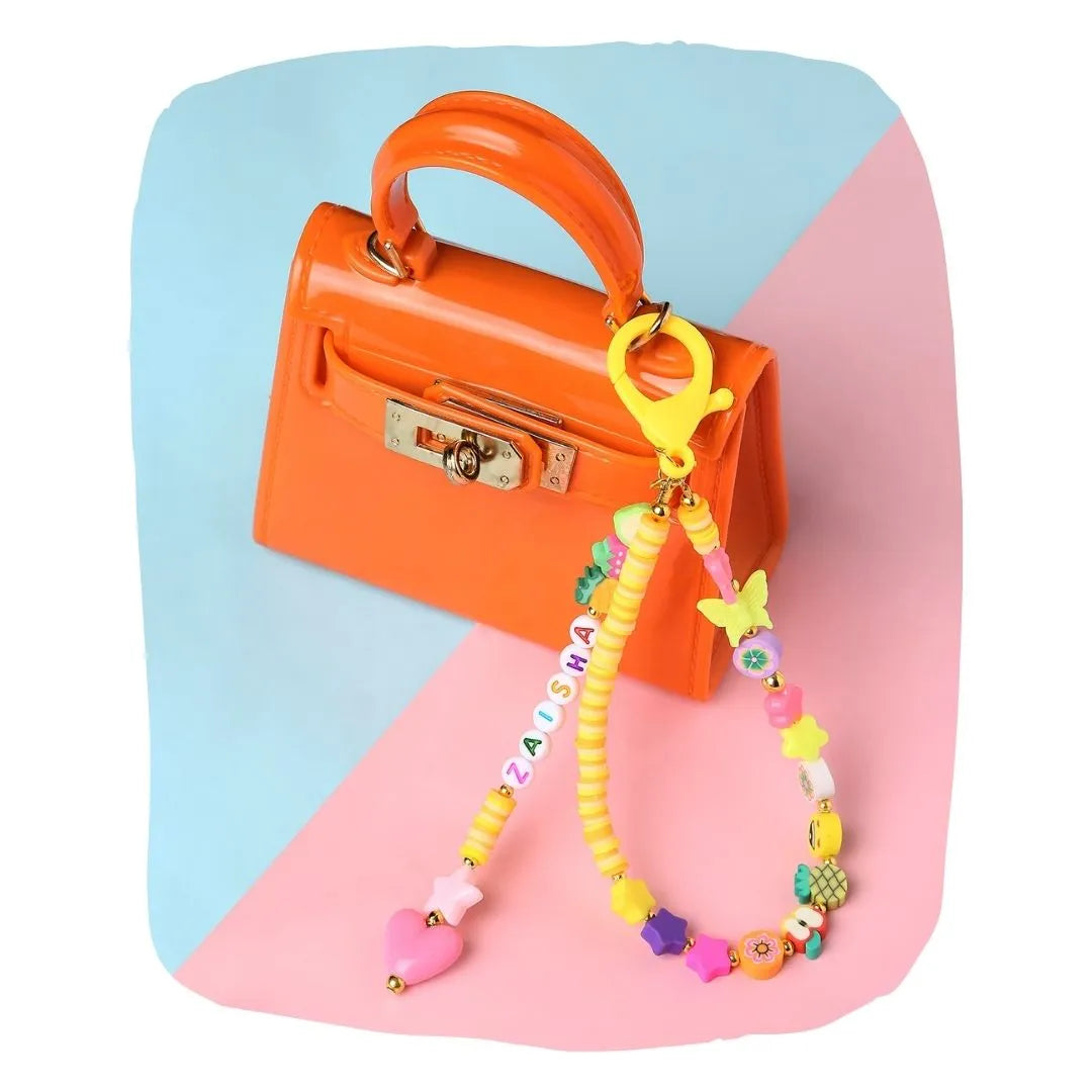 Orange bag charm personalized for kids with colorful beads and name letters, clipped to a mini orange handbag for stylish accessorizing.