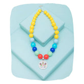 Unicorn necklace for kids with pastel beads in yellow, blue, and red, displayed on a light blue platform. Ideal magical jewelry gift.