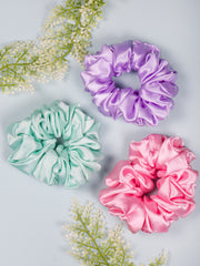 Silk Satin Hair Scrunchies in mint, lavender, and pink, displayed on a light blue background with decorative greenery.