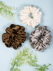 Silk Satin Scrunchies in ivory, bronze, and silver displayed on a blue background. Smooth, no-pull hair holders for day and night wear.