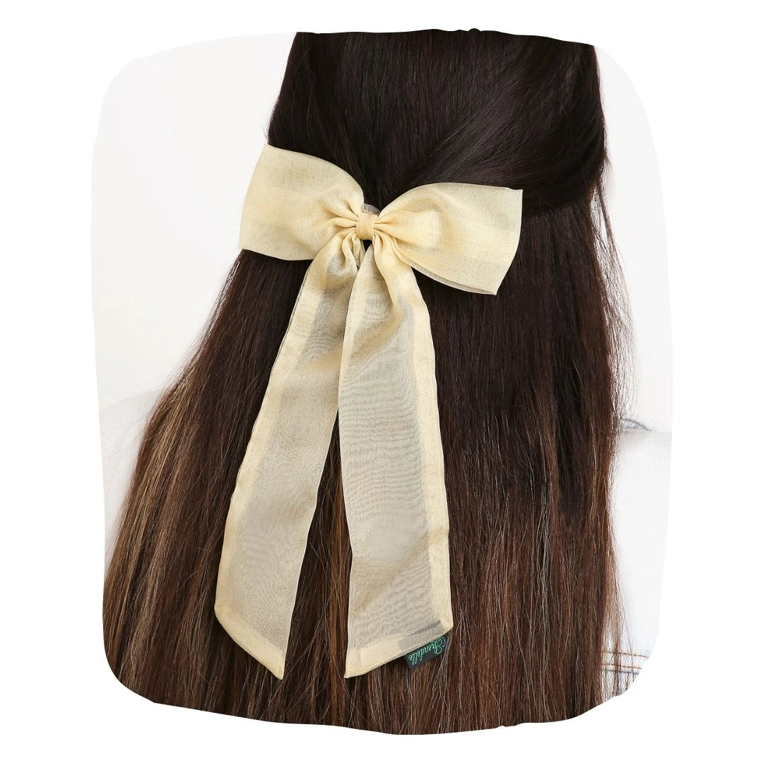 Large organza hair bow in beige with long tail, styled on dark brown hair for an elegant and classic look.