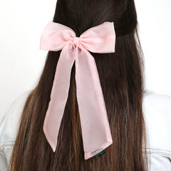 Elegant large pink organza hair bow with long tail, worn on half-up hairstyle for a soft, feminine touch.