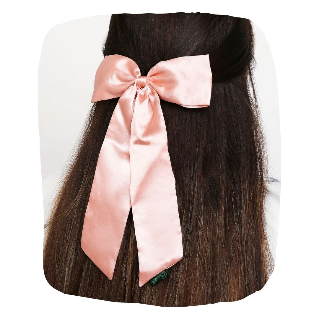 Large pastel pink satin silk hair bow styled on long dark hair. Elegant accessory with secure clip for girls' hairstyles.