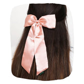 Large pastel pink satin silk hair bow styled on long dark hair. Elegant accessory with secure clip for girls' hairstyles.