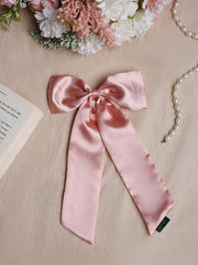 Pastel pink satin silk hair bow with long tails placed on beige fabric with flowers and pearls. Elegant handcrafted hair accessory.