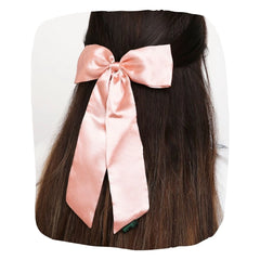 Large pastel pink satin silk hair bow styled on long dark hair. Elegant accessory with secure clip for girls' hairstyles.