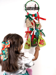 Girl reaching for a 6-Day Dreamcatcher Christmas Advent with numbered gift pouches. Personalized festive countdown decor for kids' holiday joy.