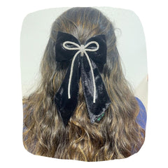 Girls black velvet hair bow with rhinestone cord, handmade and secured with a clip, styled on long wavy hair. Elegant accessory for kids.