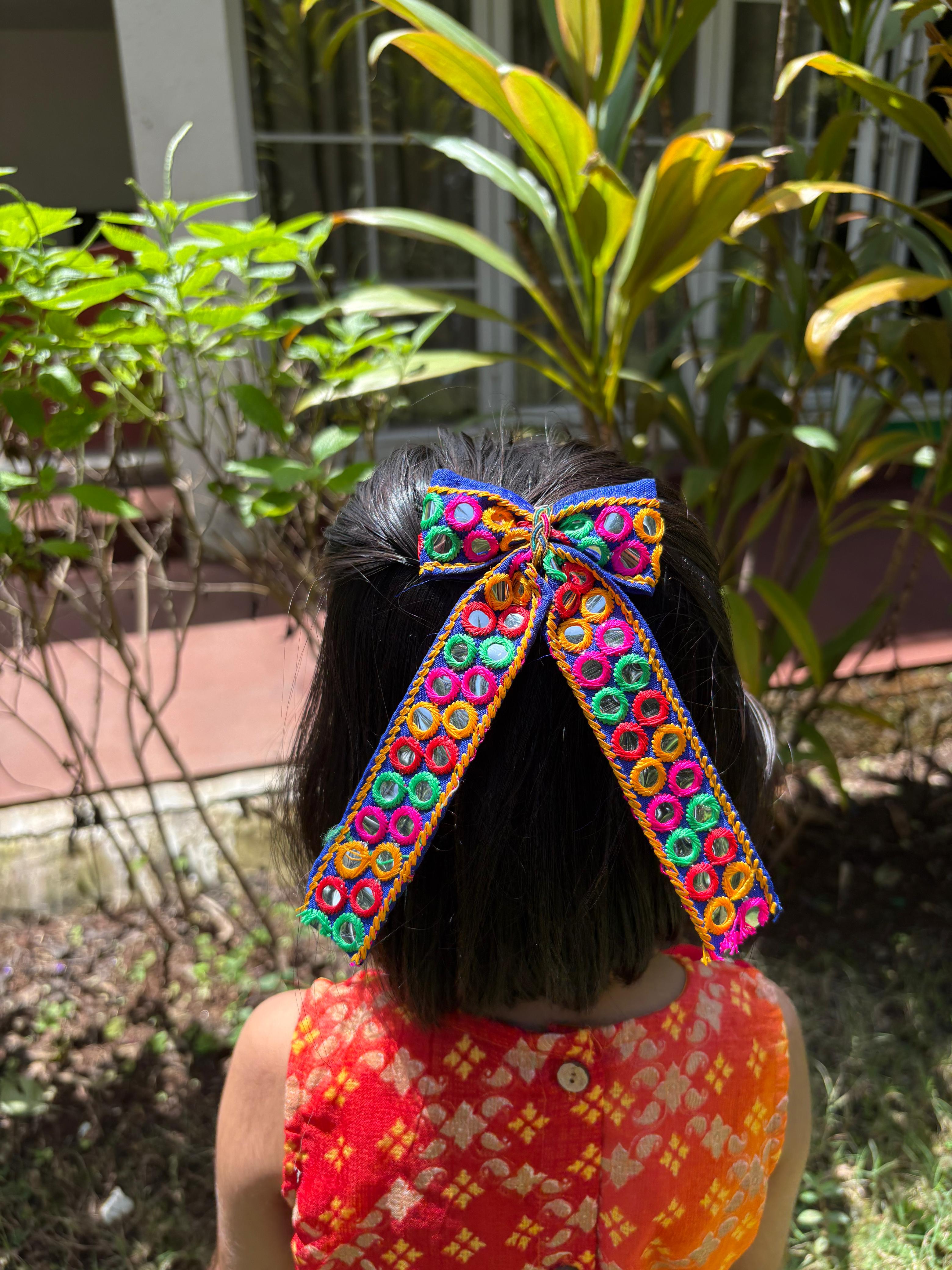 Girl wearing Dholida Pigtail Bow, a vibrant ethnic Navratri hair accessory with mirror work, perfect for festive Garba outfits.