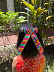 Girl wearing Dholida Pigtail Bow, a vibrant ethnic Navratri hair accessory with mirror work, perfect for festive Garba outfits.