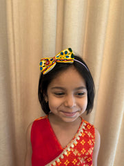 Smiling girl in festive attire wearing Kesariyo Hairband, a handcrafted Navratri accessory with colorful mirrors, tassels, and bead detailing.