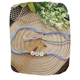 Name Rakhi gift for brother featuring multicolor thread with 'JAI' letter beads and gold accents, displayed on rustic wood with floral decor.