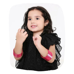 Young girl wearing Arendelle Kids hot pink metal bangles set of 36, styled with a black dress for a bold ethnic look.