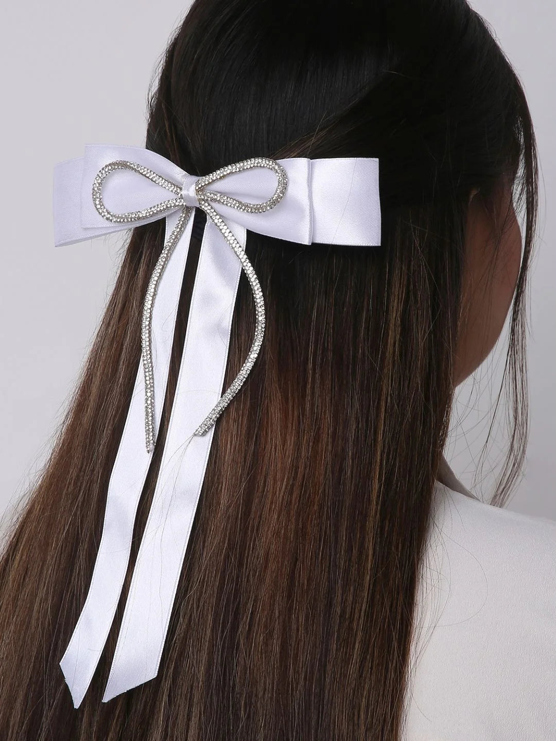 White satin hair bow with rhinestone detail worn on straight hair. Secure and colorful accessory for kids and women.