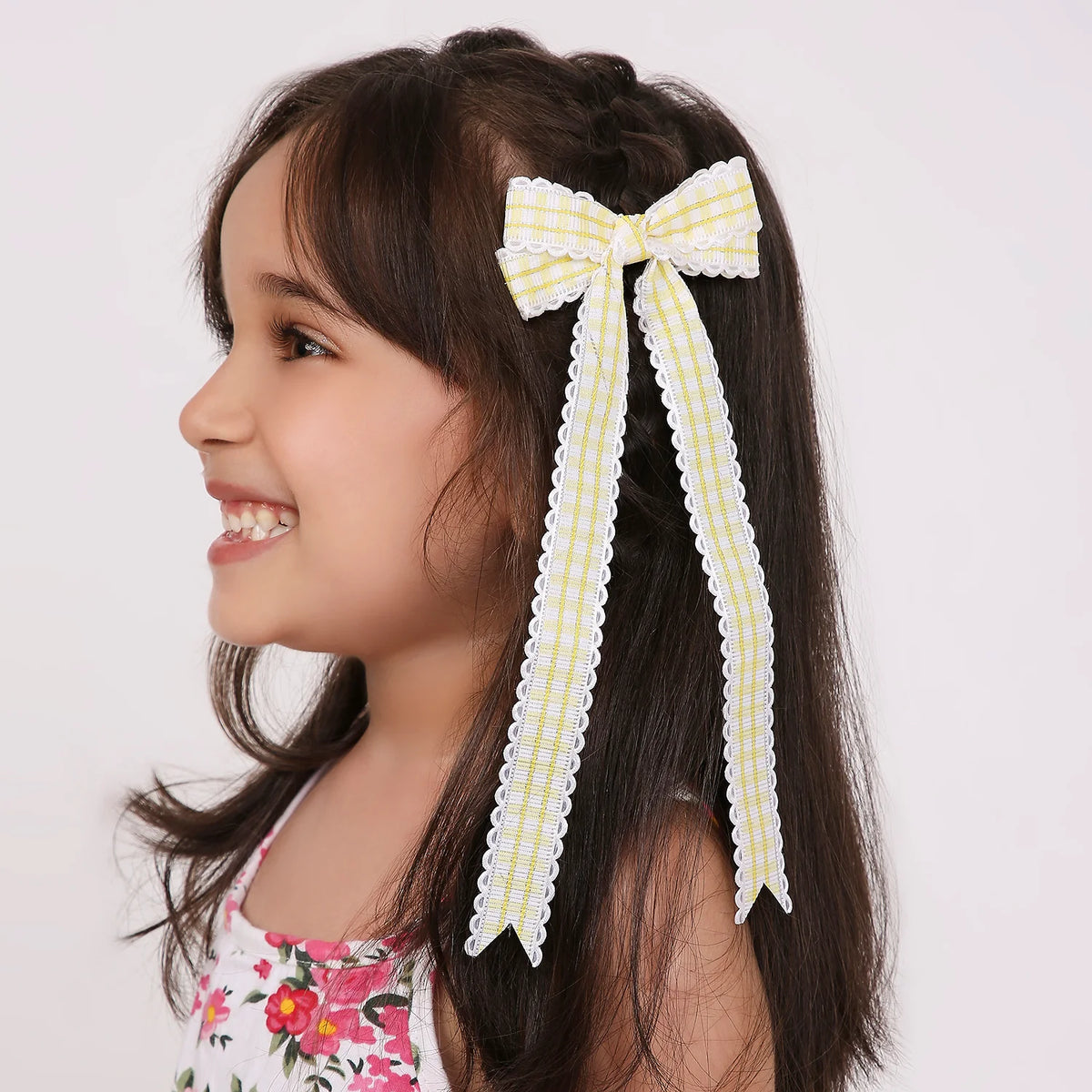 Girl wearing yellow checks ribbon long tail hair bow with scalloped edges. Bright and cheerful ribbon hair accessory for girls.