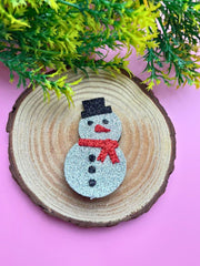 Festive Glitter Foam Snowman Hair Clip displayed on wooden base with holiday greenery, great for Christmas styling.