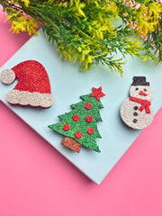 Christmas Glitter Hair Clips for Girls displayed on pastel background with greenery, featuring festive tree, Santa hat, and snowman shapes.