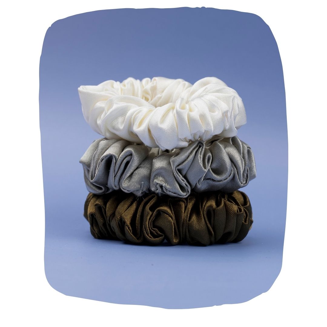 Silk satin hair scrunchies pack in white, silver, and brown stacked on blue background. Eco-friendly and gentle hold for all hair types.