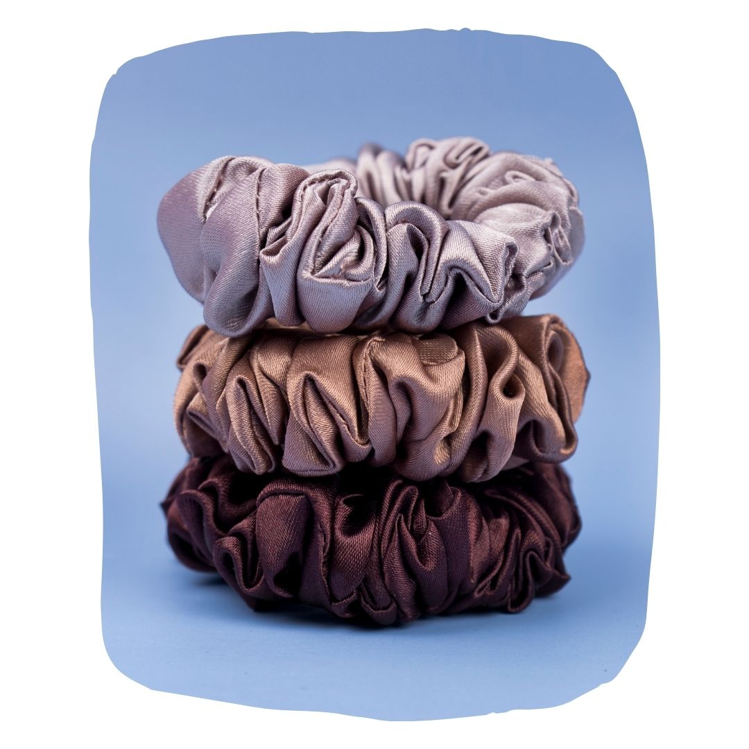 Pack of 3 satin scrunchies in mauve, bronze, and plum shades stacked on blue background. Satin Scrunchies - No Hair Breakage | Silk Comfort.