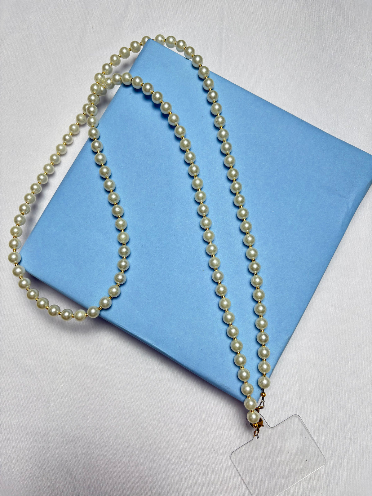 Navratri Pearl Phone Sling with white pearls displayed on a blue gift box, perfect for festive traditional outfits.