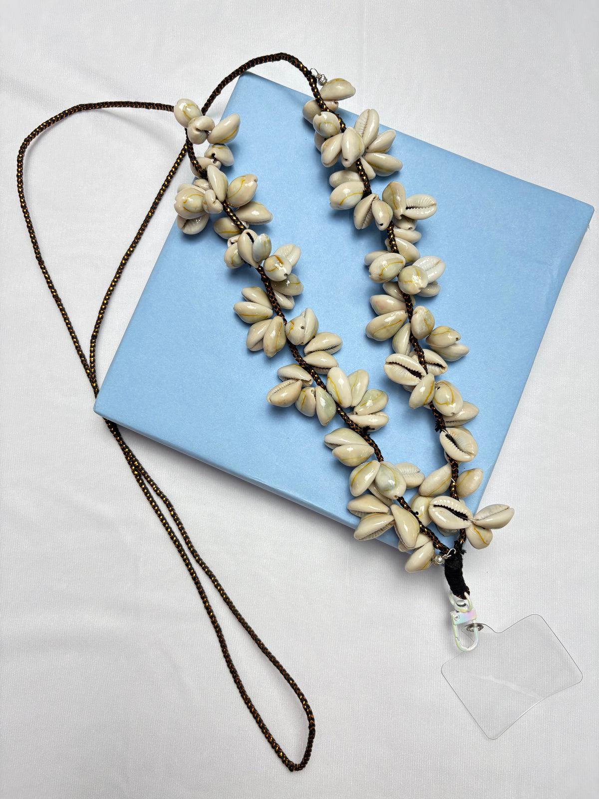 Arendelle Phone Sling - Navratri Special with cowrie shells and beaded detailing, displayed on a blue box. Ideal for ethnic festive wear.
